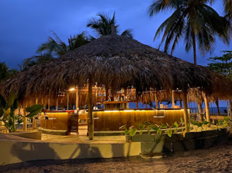 Beach restaurant with a palm-thatched roof surrounded by tropical vegetation
